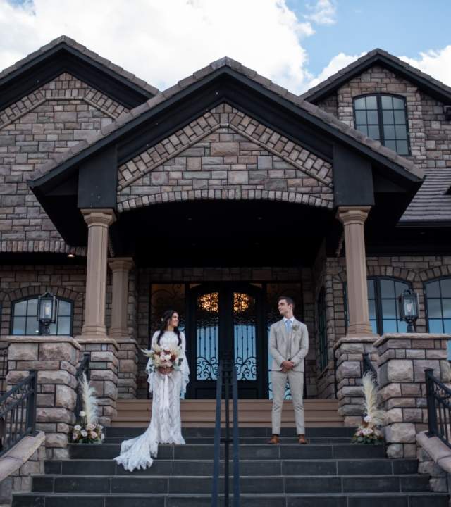 Couple stands on the front porch of the Cedar Rose Estate wedding venue in Parowan, Utah.