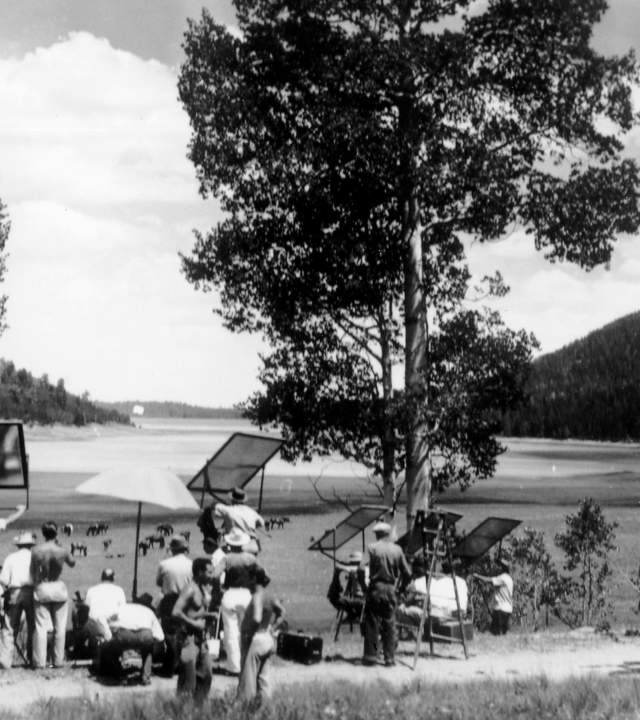 Greyscale photograph of a film crew on Cedar Mountain set up in front of a meadow framed by sloping hills and horses in the background.