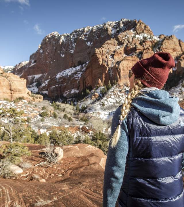 Woman dressed for colder weather hiking into red rock formations in Kolob Canyons, the North Side of Zion National Park.